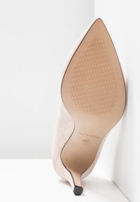 Chaussure à talon haut beige à bout pointu, inclinée pour montrer la semelle avec grip texturé et marquage de taille sur fond blanc.