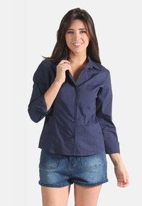 Chemise bleu marine à boutons en tissu doux, dotée d'un col, de manches longues et d'un ourlet courbé. Associée à un short en denim.