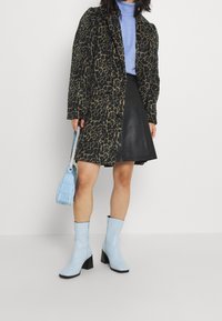 Manteau à imprimé léopard, col roulé bleu clair, jupe en cuir noir, bottes montantes bleu clair à talons blocs, et sac à main bleu texturé.