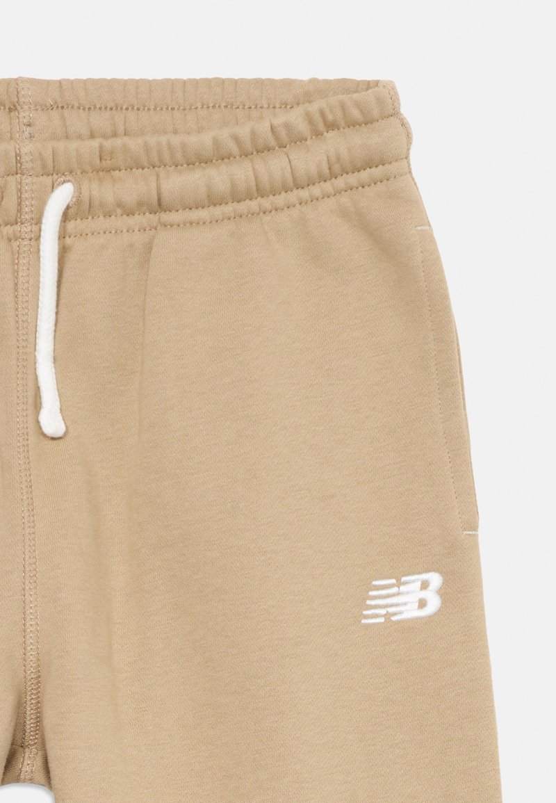 Hellbraune Jogginghose mit elastischem Bund, verstellbarem weißen Kordelzug und weißem "NB"-Logo am unteren linken Bein. Weicher Stoff.