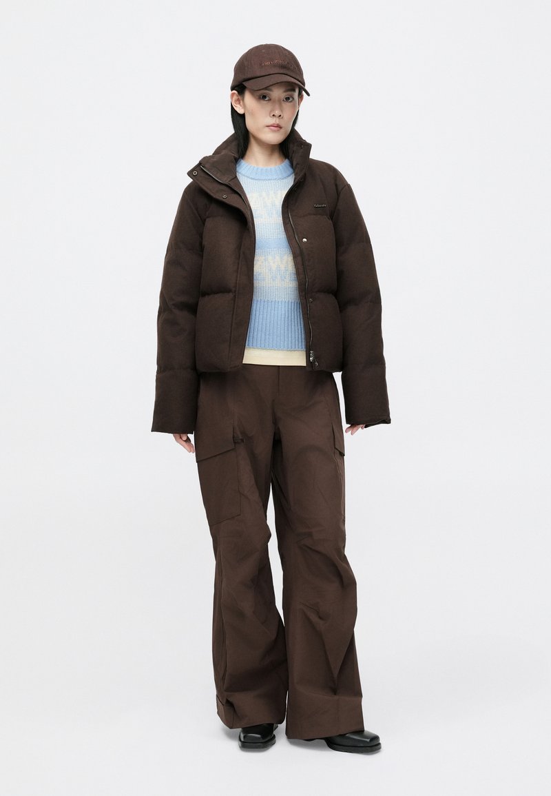 Brown puffer jacket with a high collar, light blue sweater, and brown wide-leg pants. Caps with logo detail, smooth texture throughout.