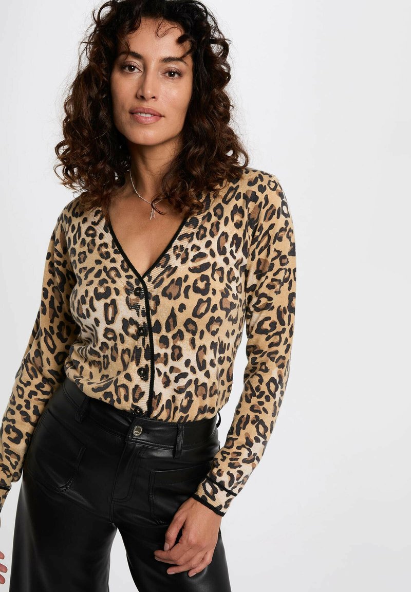 Cárdigan de estampado de leopardo en beige con acentos negros, escote en V, cierre de botones y mangas largas, combinado con pantalones de cuero negros.