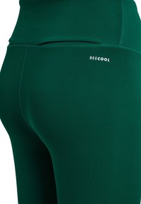 Hoge taille, donkergroene leggings gemaakt van soepel, rekbaar materiaal. Bevat discrete "BECOOL" branding en platte naden voor comfort.