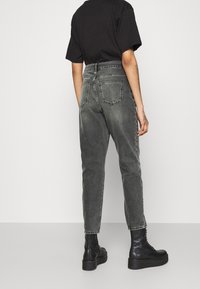 Jeans de denim negros de cintura alta con un acabado desgastado, que cuentan con cinco bolsillos y un diseño de pierna recta. Combinados con botas de combate negras.