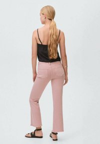 Svart linne, rosa utsvängda jeans med fransad fåll, bärs med svarta sandaler, sedd bakifrån mot en ljusgrå bakgrund.