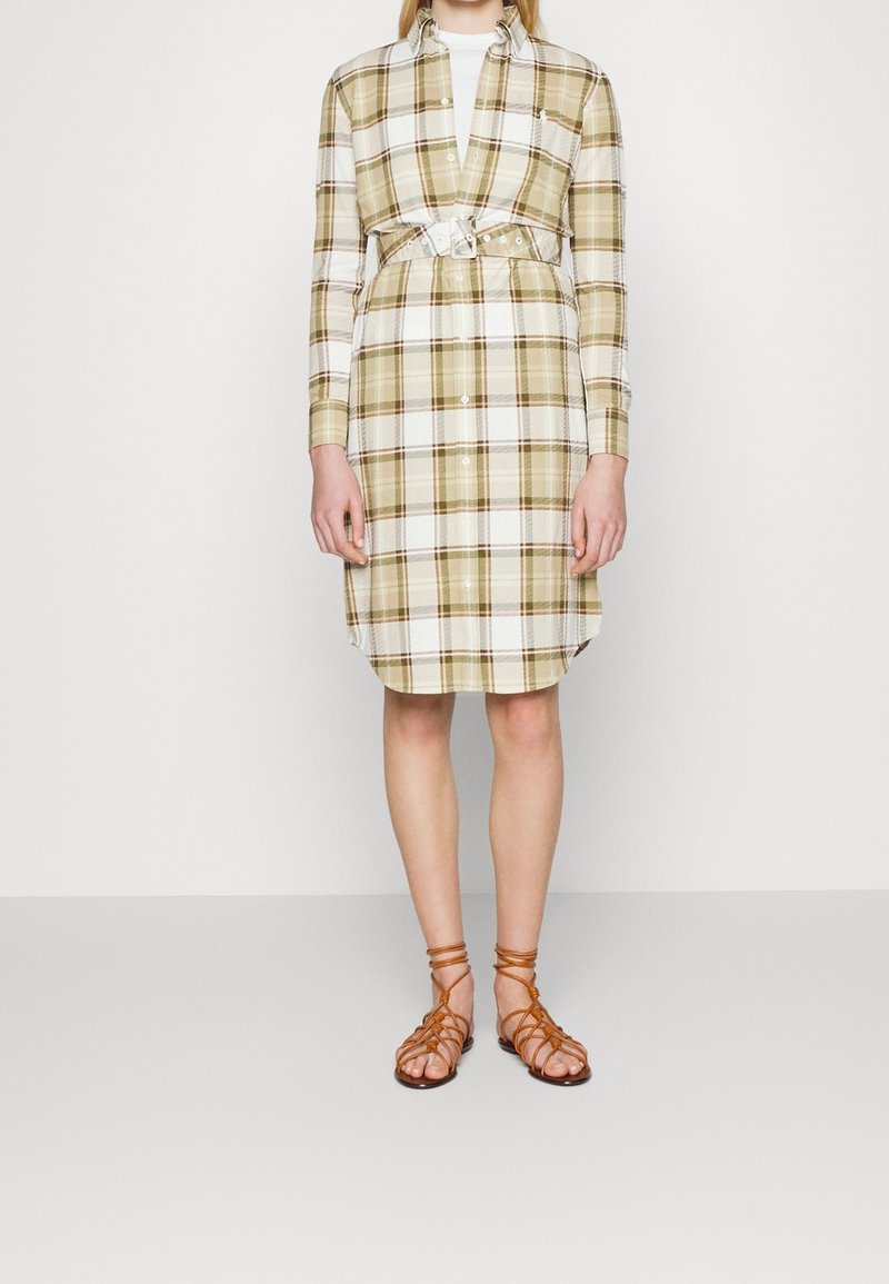 Abito camicia lungo a quadri in beige e bianco, con vita regolabile e chiusura a bottoni. Abbinato a sandali marroni con cinturini.