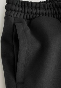 Black jogger pants made of soft, stretchy fabric. Features an elastic waistband and side pockets. Smooth texture with no visible patterns.