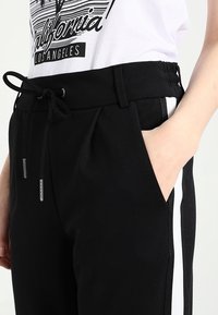 Svarta joggers med resårmidja och dragsko, sidofickor och kontrasterande vita ränder längs yttersemmarna.