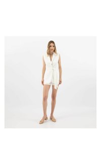 Romper bianco senza maniche con scollatura a V profonda e cintura annodata in vita. Tessuto morbido e lunghezza corta, abbinato a scarpe chiare.