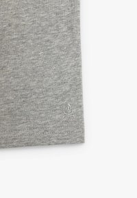 Tejido gris con un pequeño bordado de una calavera y tibias cruzadas cerca del borde inferior sobre un fondo blanco liso.