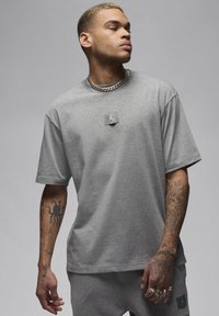 Grå t-shirt med korta ärmar, tillverkad av en bomullsblandning, med en subtil logotyp på mitten och avslappnad passform. Stylad med matchande grå underdelar.