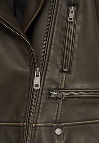 Tmavě olivově zelená kožená bunda s několika stříbrnými zipy, klopovým límcem a složitým prošíváním po látce.