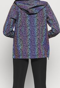 Färgglad huva jacka med ett flerfärgat geometriskt mönster på en mörk bakgrund. Lätt material med elastiska ärmslut och justerbar nederkant.