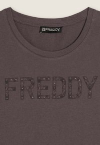 Camiseta gris oscura con cuello redondo que presenta la palabra "FREDDY" en grandes letras de lentejuelas en la parte delantera. Tejido de algodón.