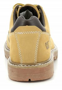 Zapato de cuero marrón con un cuello acolchado negro contrastante, costuras blancas y una suela de goma texturizada. Presenta un sistema de cordones amarillo.