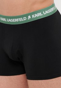 Črne bombažne bokserice z zelenim elastičnim pasom in belim napisom "KARL LAGERFELD" ter logotipom. Gladka tekstura.