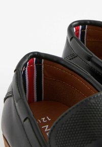 Chaussures slip-on en cuir noir avec un panneau texturé et un intérieur marron. La doublure intérieure présente des rayures rouge, blanche et marine.