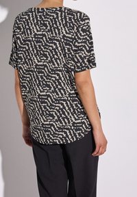 Svart och beige kortärmad topp med ett vågigt abstrakt mönster, med avspänd passform och rundad nederkant. Tillverkad av lätt tyg.