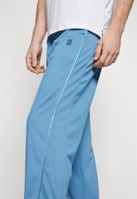 Pantalones deportivos para hombre en azul claro con franjas laterales blancas, que ofrecen un ajuste cómodo y una tela ligera para mayor movilidad.