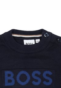 Pull en maille marine avec col côtelé et accents de boutons. Présente le logo bleu "BOSS" à l'avant. Texture douce et coupe ajustée.