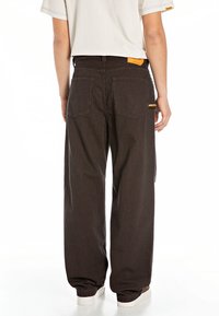Person wearing black and orange thin striped loose pants with back pockets, paired with a white short-sleeve shirt and white sneakers.