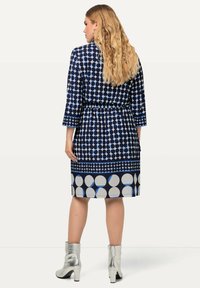 Abito navy con motivi circolari bianchi e azzurri chiari, maniche 3/4, vita cinchata, abbinato a stivaletti metallici argento alla caviglia.