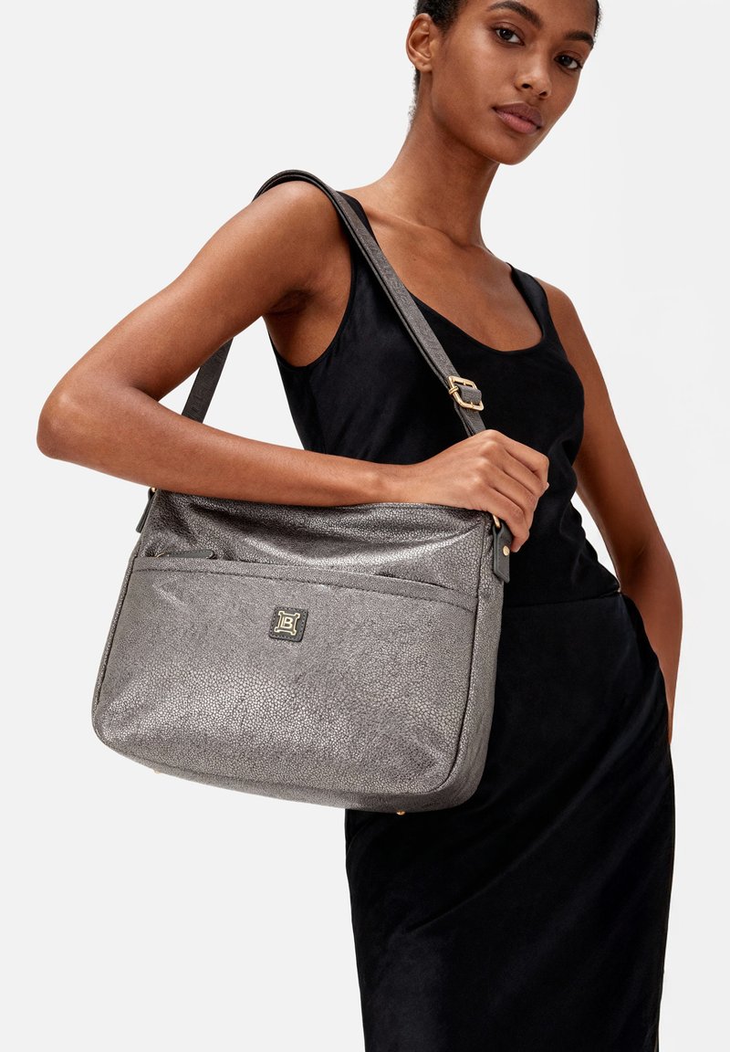 Borsa a tracolla in pelle grigia con texture, dotata di una tracolla, dettaglio in metallo dorato e una tasca frontale con zip. Design liscio e strutturato.