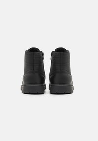 Botas de cuero negras hasta el tobillo con un acabado liso, que cuentan con cremalleras laterales, detalles de costura y una suela de goma texturizada.