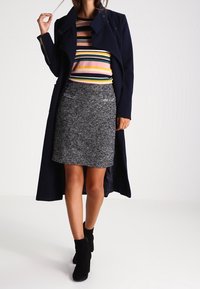 Marinblå trenchcoat, flerfärgad randig skjorta, grå texturerad kjol, ankelskor. Anmärkningsvärda detaljer: fickor på kjolen, lager-på-lager-effekt.