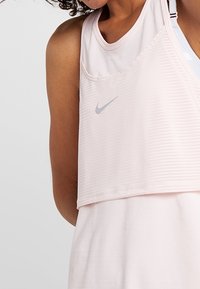 Top sportivo rosa chiaro con design testurizzato, logo Nike in argento e spalline regolabili. Il tessuto sembra morbido e traspirante.