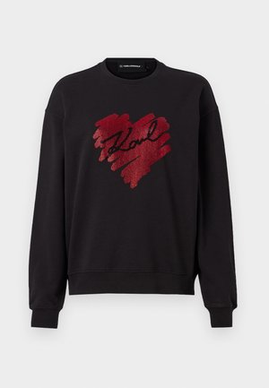 Svart hettegenser med lange ermer, prydet med et rødt glitterhjerte-design og navnet "Karl" i kursiv. Myk stoff, ribbede mansjetter og kant.