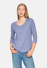 Hellblaues, langärmeliges Oberteil mit Rundhalsausschnitt. Glatte Textur, lässige Passform, kombiniert mit blauen Jeans für einen entspannten Look.