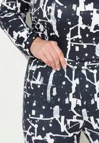 Abbigliamento attivo in bianco e nero con motivi, caratterizzato da schizzi e linee astratte, con un design aderente e tessuto testurizzato. Polsini e vita dettagliati.