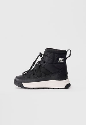 Botte d'hiver imperméable noire avec semelle blanche, fermeture à lacet à tirage, et logo Sorel sur la cheville, présentée en profil latéral sur fond blanc.