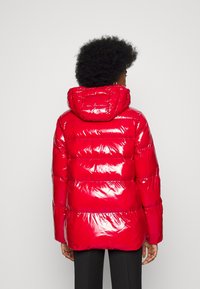 Chaqueta acolchada roja y brillante con capucha, que presenta un diseño acolchado y un corte de longitud media. La superficie texturizada realza el aspecto general.