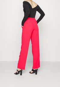 Röda vida byxor med elastisk midja, kombinerade med en svart off-shoulder topp. Svarta högklackade sandaler synliga på fötterna.