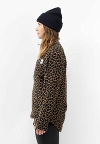 Luipaardprint fleece jasje met lange mouwen, een hoge kraag en een relaxte pasvorm. Gecombineerd met een zwarte gebreide beanie.