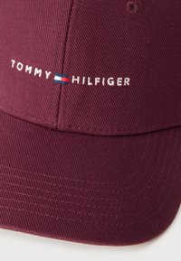 Burgundia puuvillast tekstuuriga pesapalli nokamüts. Omadused valge tikitud kaubamärgi nimega "TOMMY HILFIGER" ja väike logoaksent.