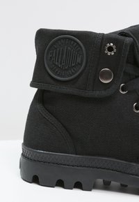 Bottines chelsea noires en toile avec œillets métalliques, semelle en caoutchouc et un patch rond en caoutchouc avec le logo "PALLADIUM". Détails texturés sur le dessus.