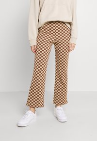 Brun och beige rutig vida byxor gjorda av mjuk tyg, kombinerat med vita sneakers och en beige hoodie.