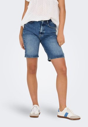 Shorts en denim dans un délavage bleu moyen avec une coupe droite, des ourlets retroussés et un design à cinq poches, accompagnés de baskets blanches avec des accents bleus.