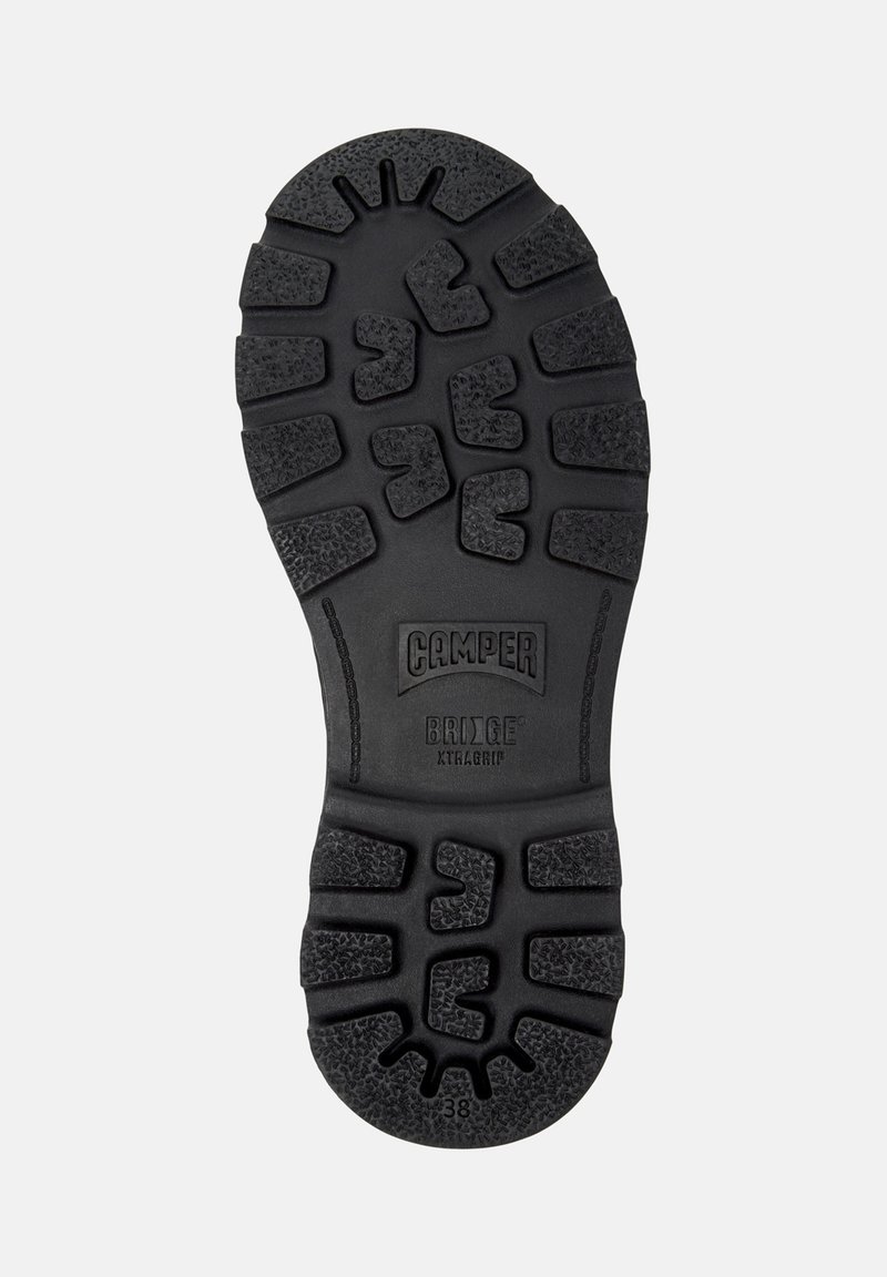 Black rubber shoe sole featuring a textured, tread pattern with grooves and rounded accents. Marked "CAMPPER BRIDGE XTRAGRIP."