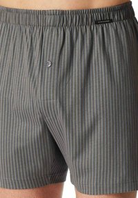 Boxers gris à rayures avec une braguette à boutons, une ceinture élastique et une petite étiquette logo ; le tissu présente une texture fine avec des accents bleus et jaunes.