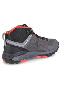 Botte de randonnée mi-haute avec une tige en suède et textile gris, accents noirs, lacets rouges, motifs texturés et une semelle robuste avec des détails orange.