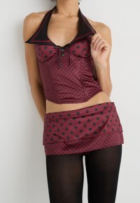 Haut halter à pois bourgogne avec des accents noirs, doté d'un col, de boutons sur le devant et d'une mini jupe assortie. Des collants noirs viennent compléter la tenue.