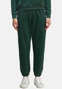 Groene joggingsbroek van zachte stof met elastische boorden, zijzakken en een relaxte pasvorm. Gecombineerd met witte sneakers.