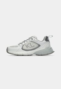 Fehér sportcipő szürke részletekkel, hálós és szintetikus anyagból, fűzős kialakítású, texturált talppal, és logóval az oldalán és a sarkán.
