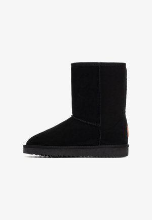 Stivale alla caviglia in suede nero con punta rotonda, suola piatta e testurizzata, e dettagli di cucitura visibili. Presenta un piccolo logo in pelle sul lato.