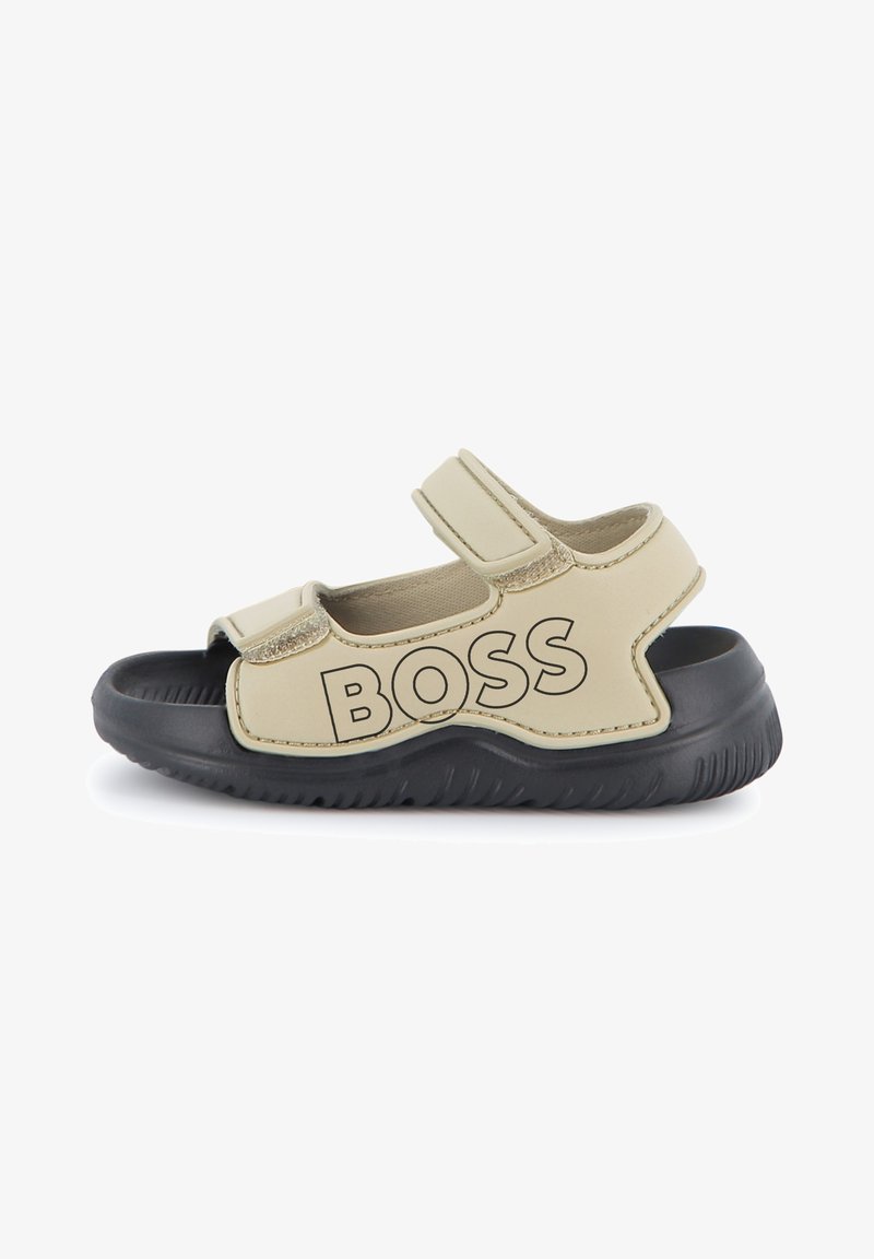 Beige Sandale mit schwarzer Sohle, verstellbaren Klettverschlüssen und prominentem "BOSS"-Logo an der Seite. Glattes Material und offenes Design.