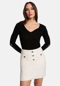 Haut long à manches ribbées noir avec un col en V et des accents de boutons aux manches, associé à une mini-jupe texturée blanche avec des boutons à l'avant et des poches.